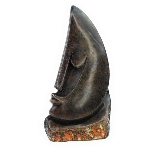 A hand-carved stone sculpture of an abstract face, with a predominantly dark color palette.