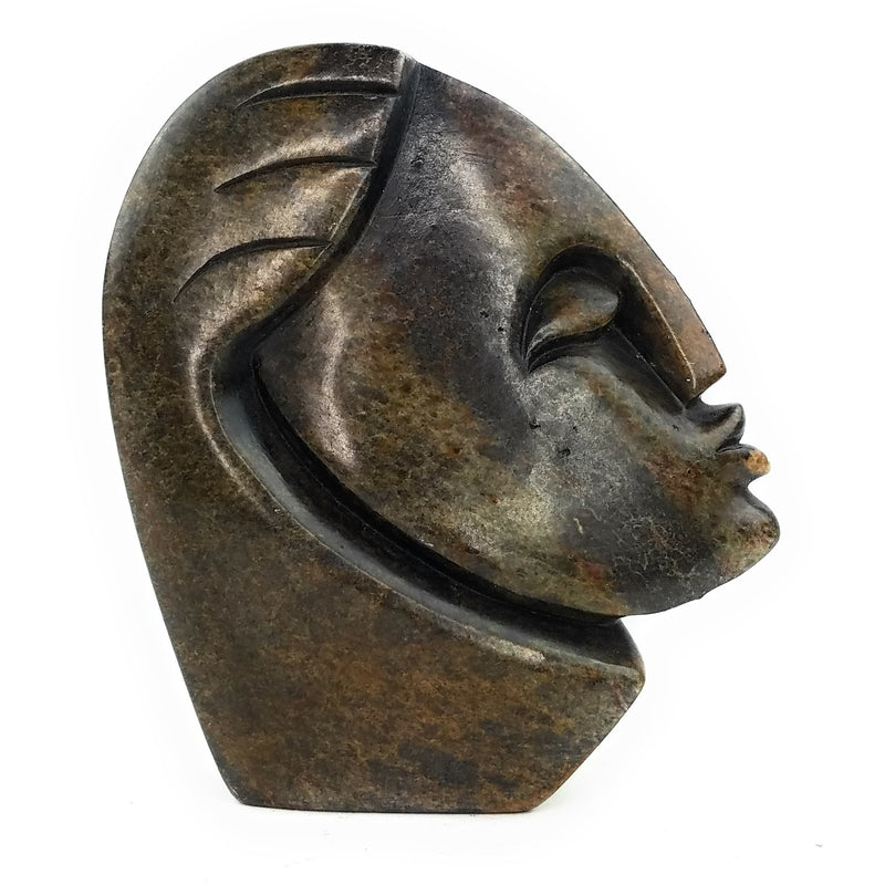 A hand-carved stone sculpture of an abstract face, with a dark, mottled appearance, indicative of the traditional Shona stone carving art form.