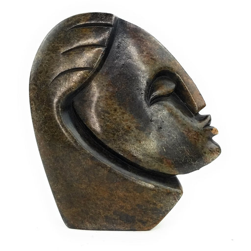 A hand-carved stone sculpture of an abstract face, with a dark, mottled appearance, indicative of the traditional Shona stone carving art form.