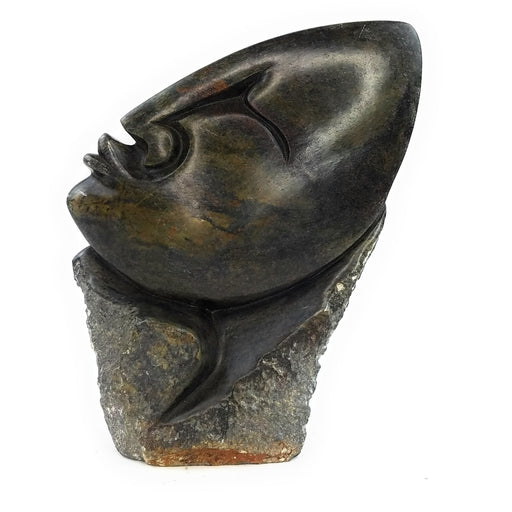 A hand-carved stone sculpture of an abstract face, predominantly dark in color.