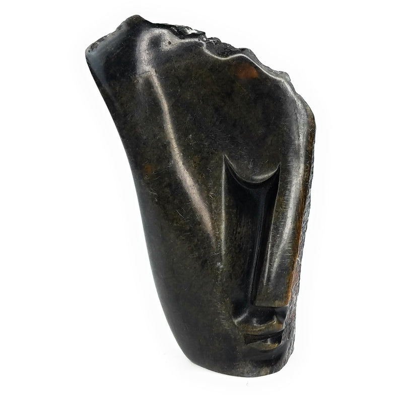 A hand-carved stone sculpture of an abstract face, with a dark, mottled appearance, indicative of the traditional Shona stone carving art.