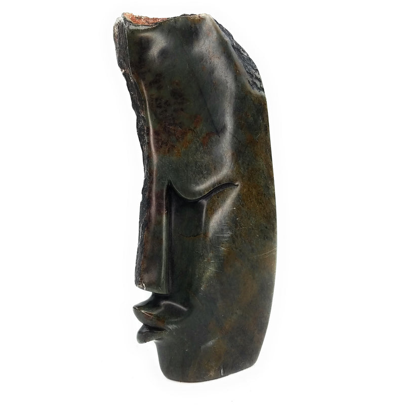 An abstract stone sculpture of a face, with a dark, mottled appearance, indicative of the Shona stone carving tradition.