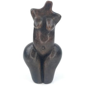 A handcrafted stone sculpture of a female torso, with exaggerated hips and breasts, on a white background.