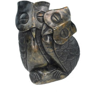 A hand-carved stone sculpture of an owl couple, with one owl perched on top of the other, set against a plain background.
