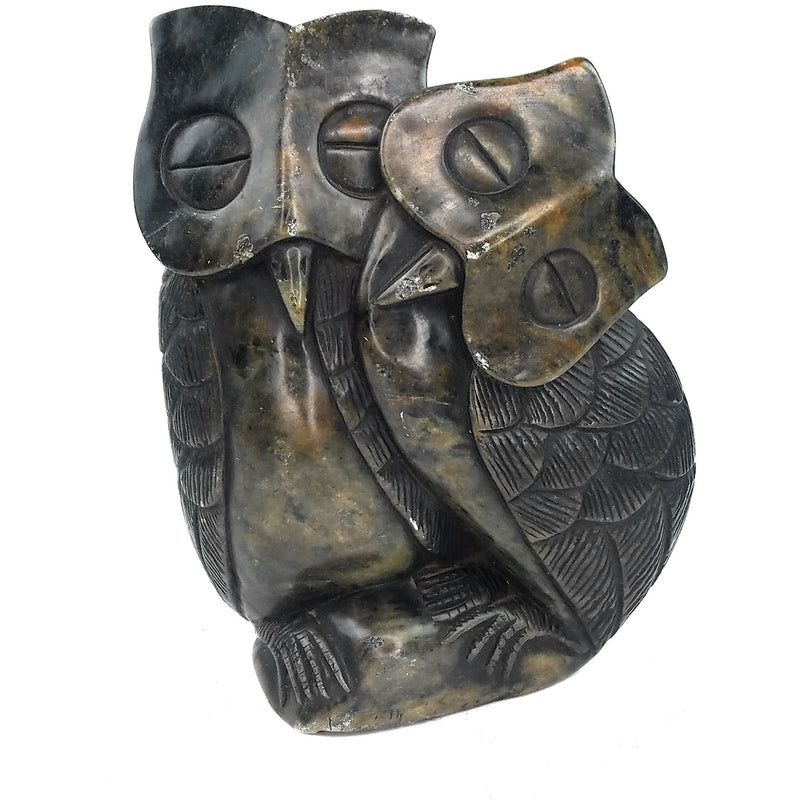 A hand-carved stone sculpture of an owl couple, with one owl perched on top of the other, set against a plain background.