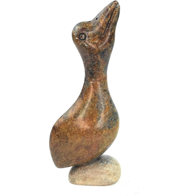 A hand-carved serpentine stone pelican sculpture, with a rough texture and a natural color palette, mounted on a small stone base.