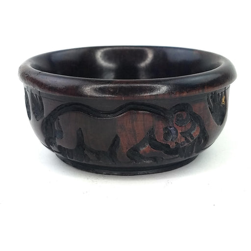 A hand-carved ebony wood bowl with animal patterns, primarily dark in color and smoothly polished on the inside.