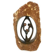A hand-carved stone sculpture depicting a family of three, with intricate details and a textured surface, primarily in brown tones.