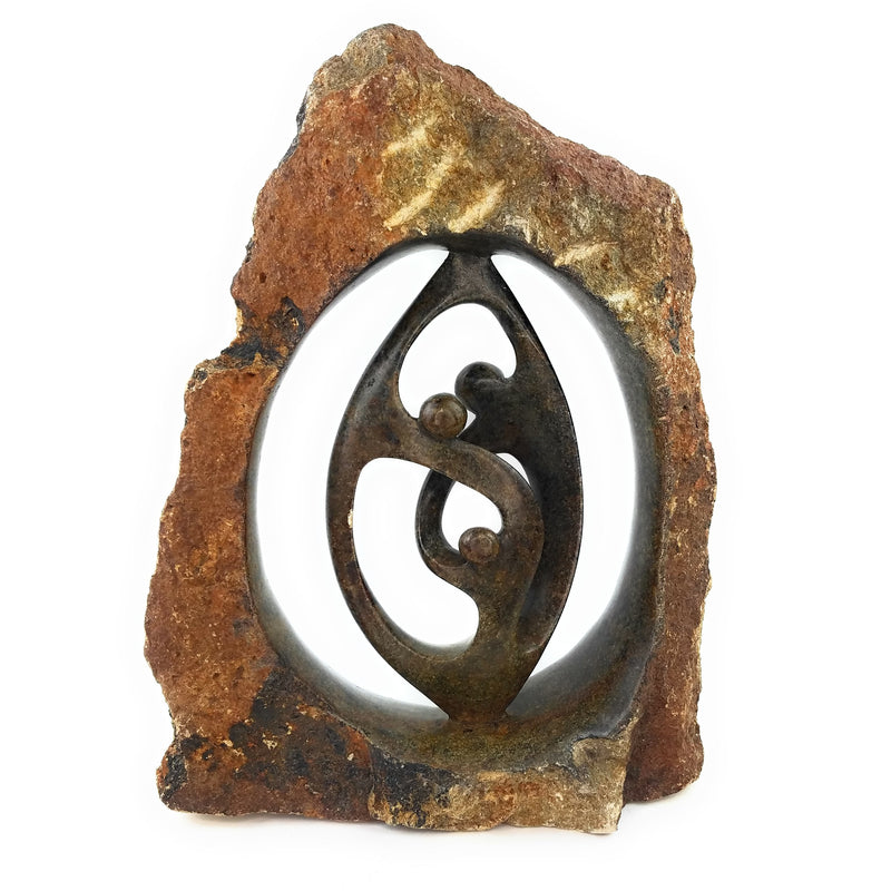 A hand-carved stone sculpture depicting a family of three, with intricate details and a rustic appearance, against a natural stone background.