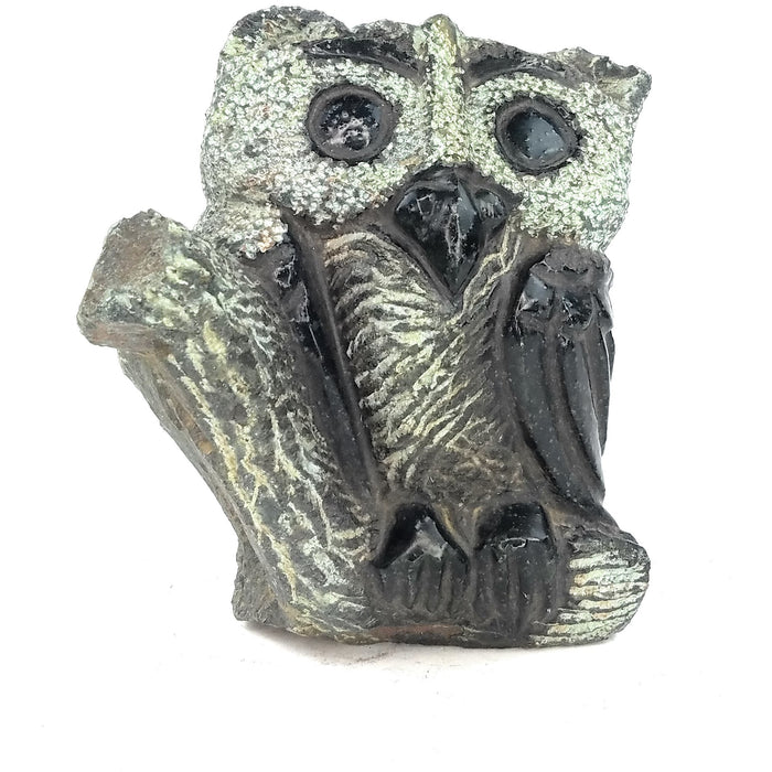 A hand-carved stone sculpture of an owl with intricate detailing and a textured surface, primarily in dark tones.